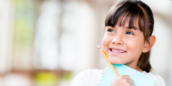 Menina de aproximadamente 6 anos segurando um caderno e um lápis