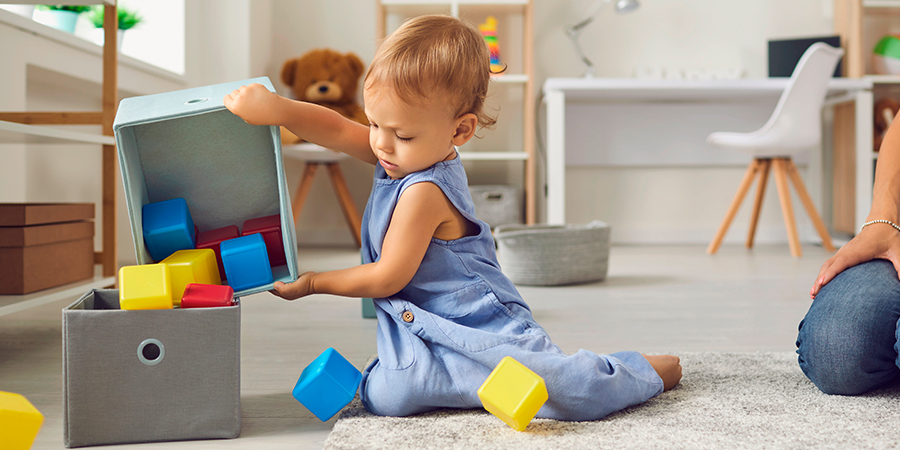 Uma criança ajoelhada no chão de uma área de brinquedos, brincando com uma caixa de cubos coloridos